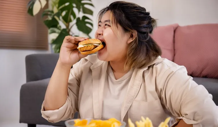 cocukluk-caginda-obezite-1-752x440-happy-asian-fat-woman-enjoy-eating-delicious-hamburger-living-room1.webp
