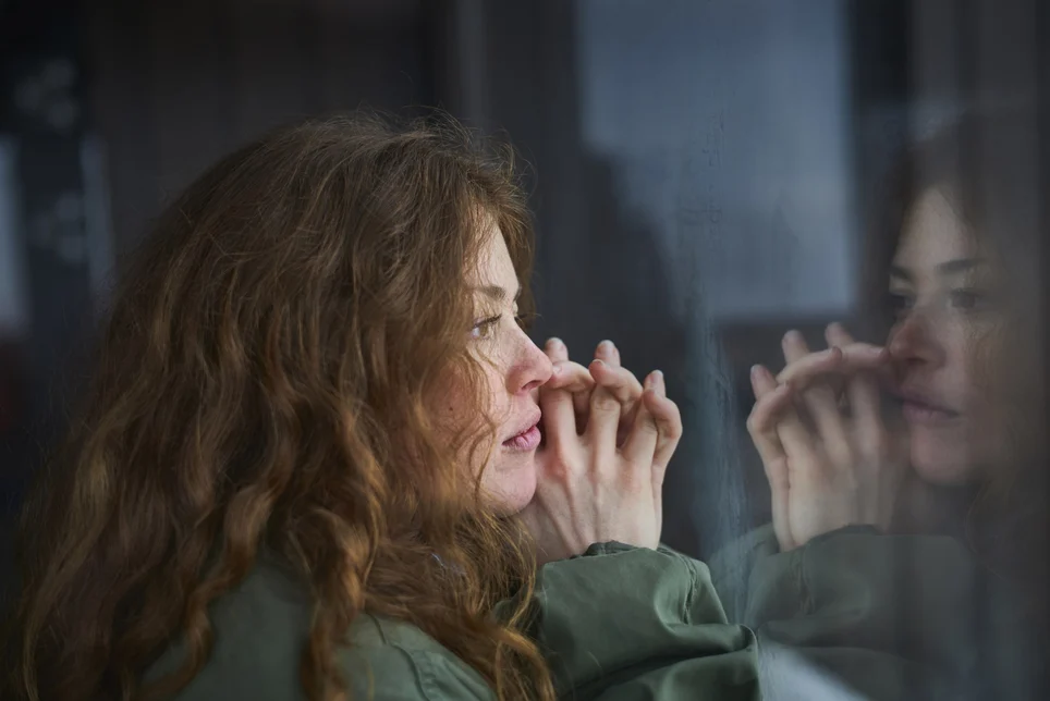 woman-looking-out-of-window-into-her-reflection.webp