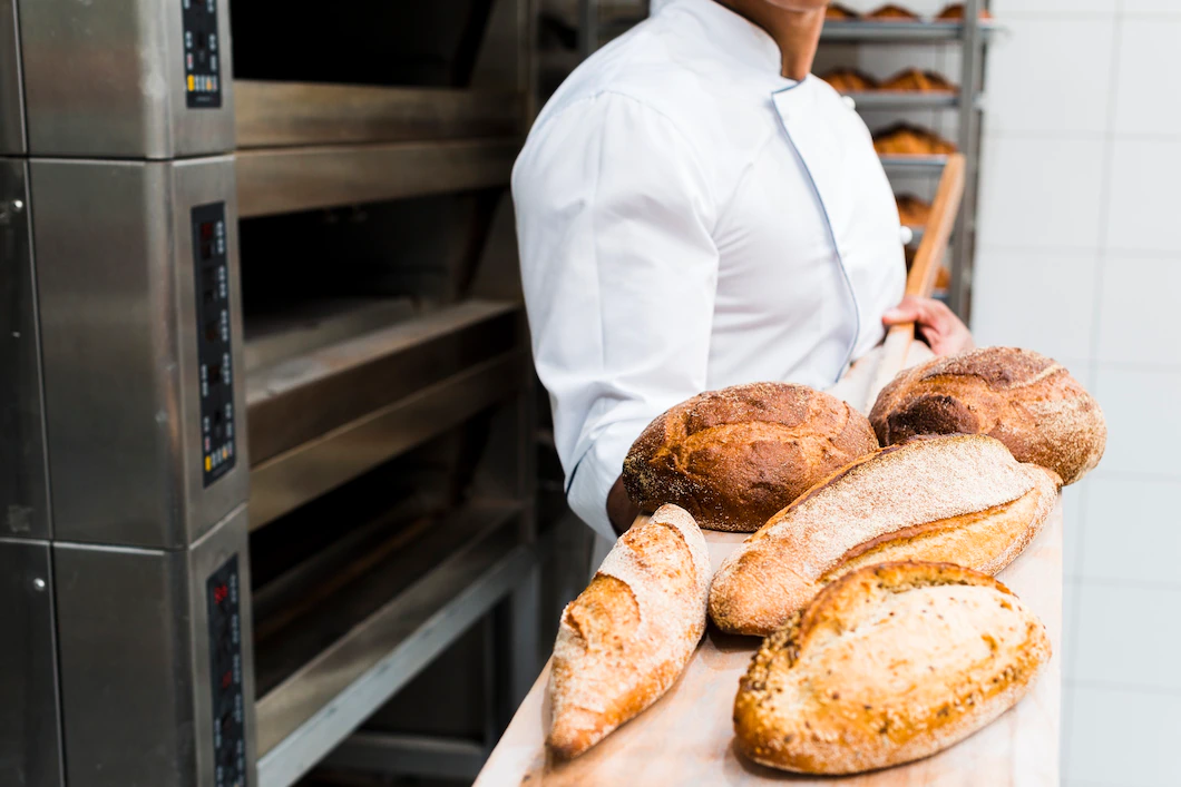 close-up-male-baker-holding-fresh-baked-bread-wooden-shovel-from-oven-23-2148189054.webp